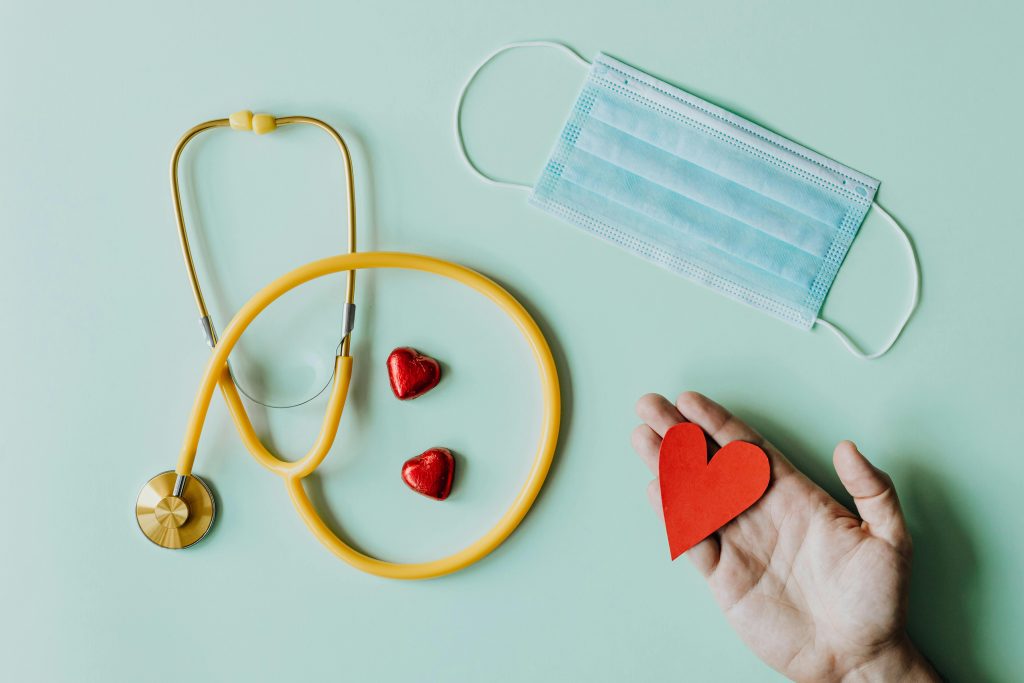 pexels-photo-4386466-4386466 Top view of crop anonymous person hand with red paper heart on table with stethoscope and medical mask for coronavirus prevention